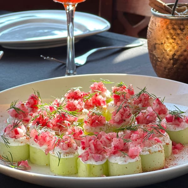 Cucumber bites topped with white cream, diced red fruit, and fresh dill on a white plate.