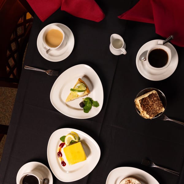Overhead view of various desserts and coffee on a black tablecloth with red napkins.