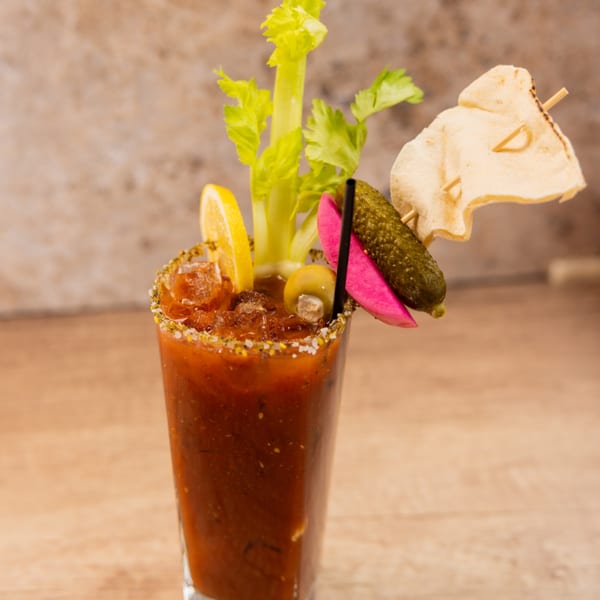 A Bloody Mary cocktail garnished with celery, lemon, olives, pickles, and a chip.