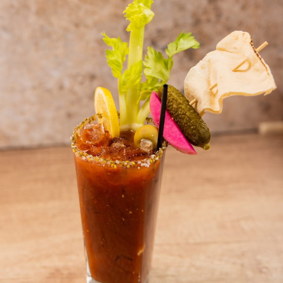A Bloody Mary cocktail garnished with celery, lemon, olives, pickles, and a chip.