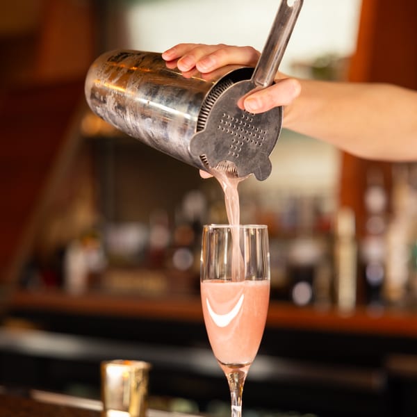 A bartender pours a pink cocktail from a shaker into a tall glass at Laziza.