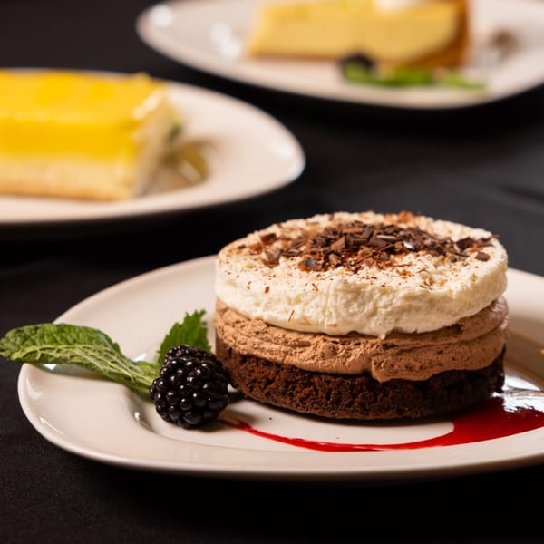 Chocolate mousse cake with whipped cream, chocolate shavings, a blackberry, and mint on a white plate.