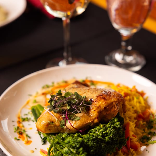 Laziza's American cuisine: a golden-brown chicken breast with sauce, microgreens, broccoli, and yellow rice.