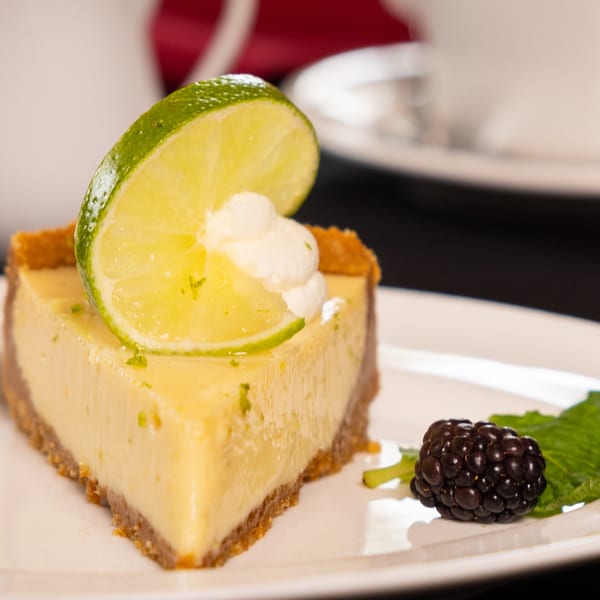 A slice of Key lime pie with whipped cream, a lime wedge, and a blackberry on a white plate.