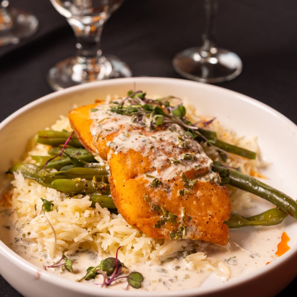 Laziza's American salmon dish with creamy sauce, green beans, and rice in a white bowl.