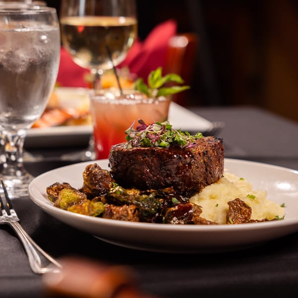A Laziza American steak entree with mashed potatoes, roasted Brussels sprouts, and drinks.