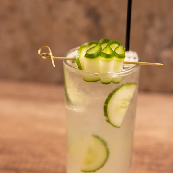 A refreshing Laziza American cocktail with cucumber slices and a black straw.