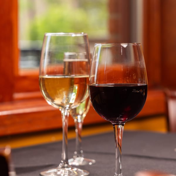 Three wine glasses, two with white wine and one with red wine, on a table at Laziza.