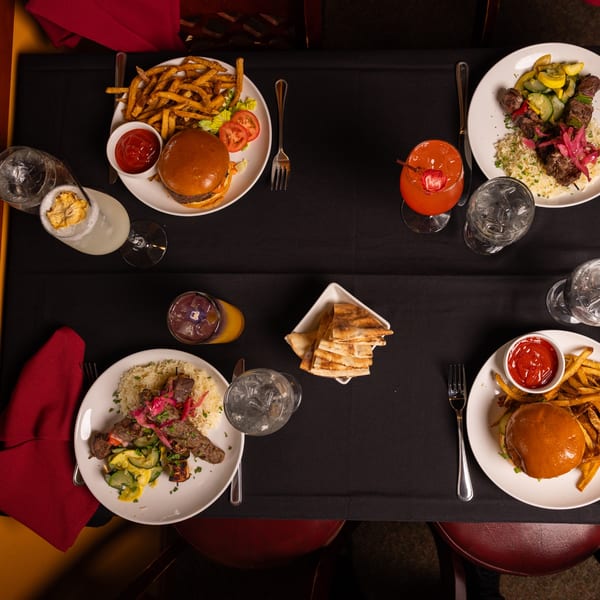 Overhead view of a table set with Laziza American burgers, fries, kebabs, rice, and cocktails.