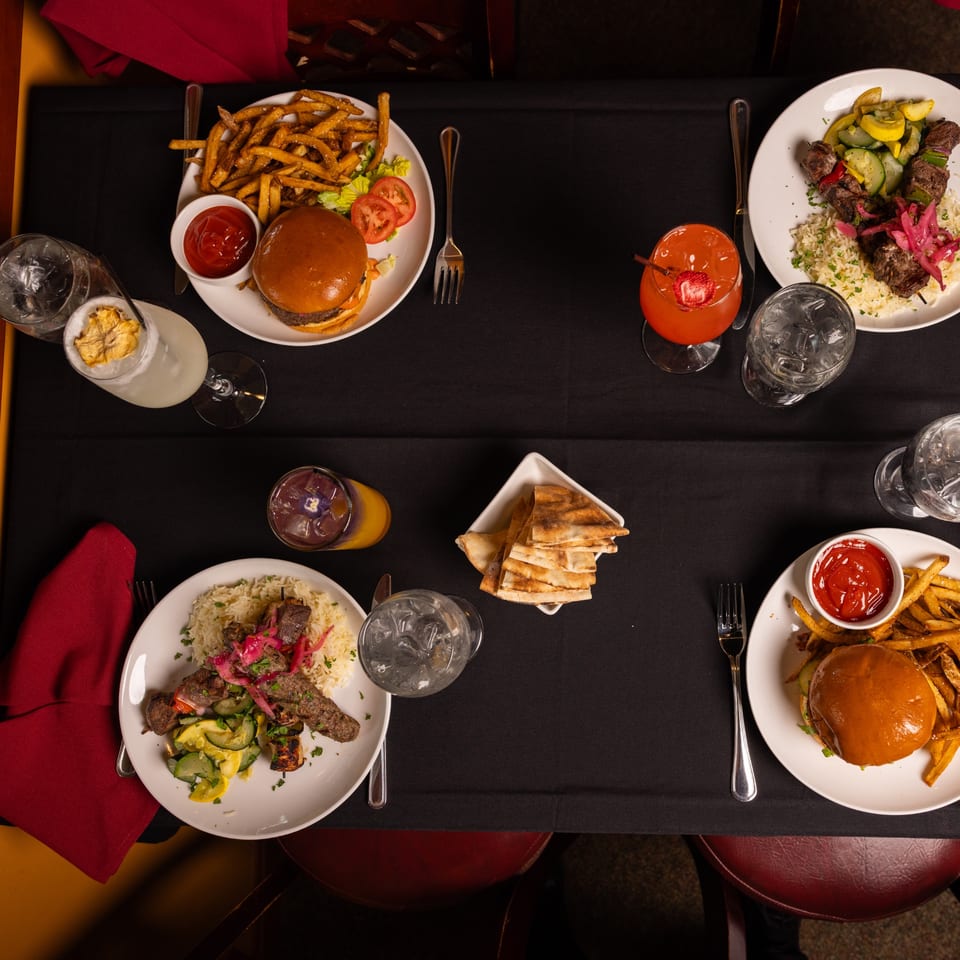 Overhead view of a table set with Laziza American burgers, fries, kebabs, rice, and cocktails.