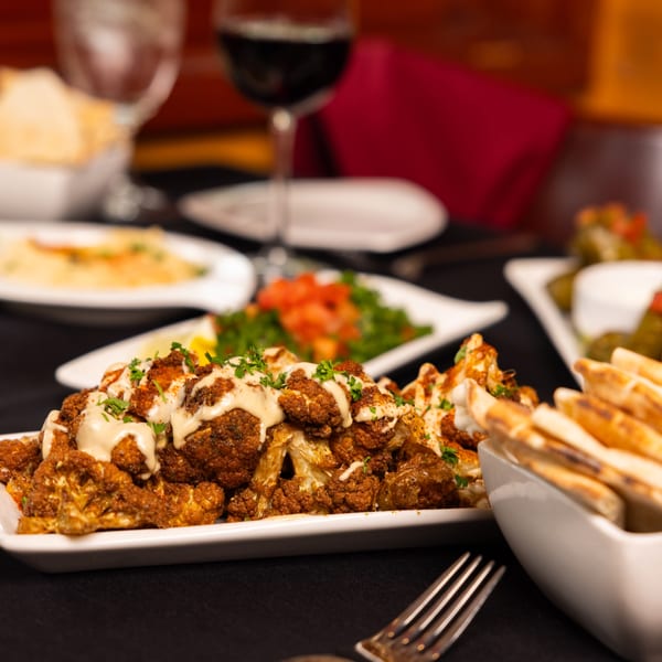 Laziza's American cuisine features a plate of roasted cauliflower with sauce, pita bread, and wine.