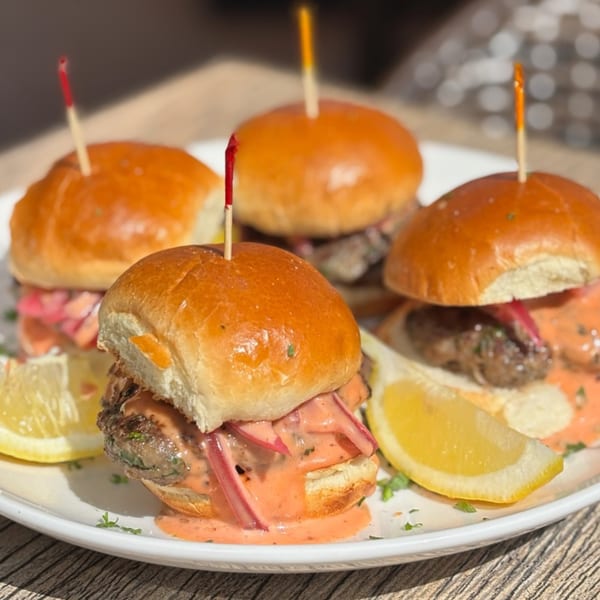 Four Laziza American sliders with sauce, red onions, and lemon wedges on a white plate.