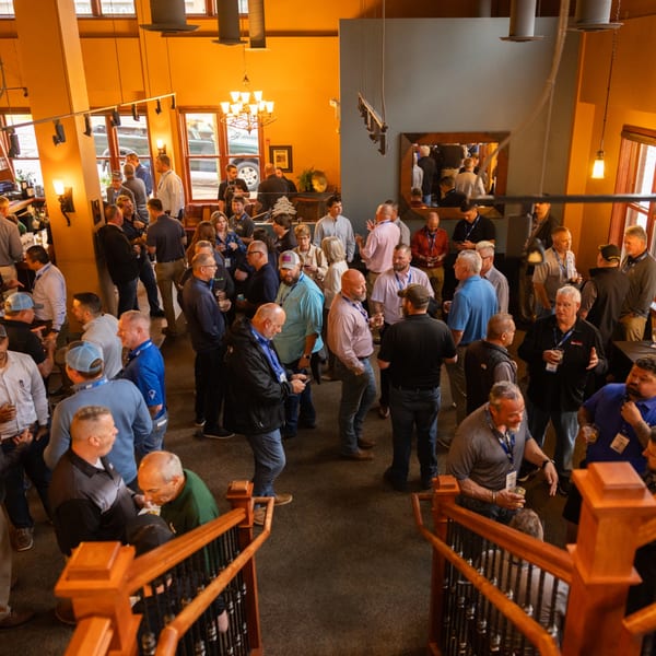 A large group of men socializing and networking in a spacious, warmly lit American restaurant.