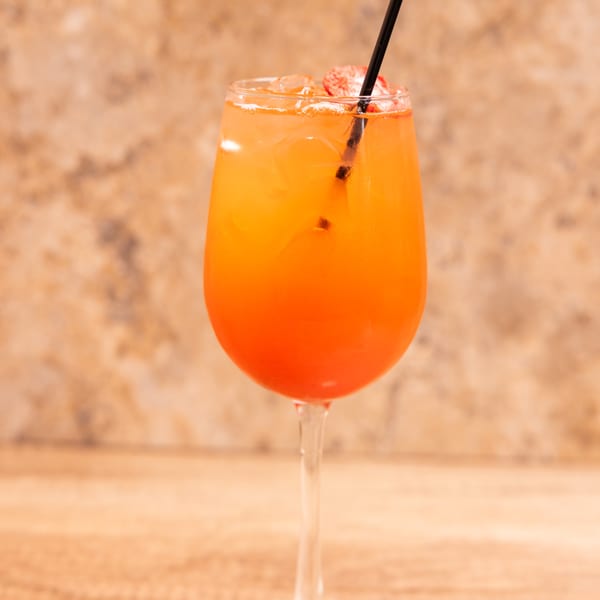 A vibrant orange and red cocktail with ice and a black straw in a wine glass.